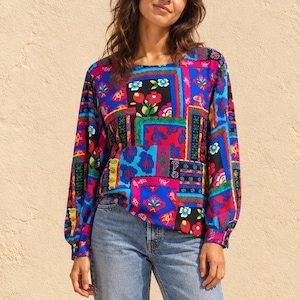 Könnte beinhalten: Eine langärmelige Bluse mit einem lebendigen Patchwork-Muster aus kräftigen Blöcken in Blau, Rot, Pink und Grün. Das Design umfasst komplexe florale Motive und geometrische Formen, die in einem farbenfrohen, mehrteiligen Layout angeordnet sind.