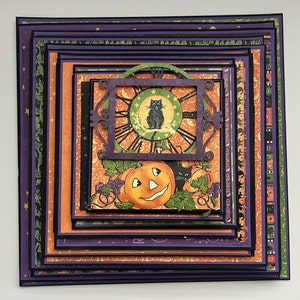 May include: A layered Halloween card with a black cat, a jack-o'-lantern, and a clock face. The card is decorated with orange, green, and purple paper and has a black frame.