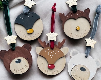 May include: Six wooden Christmas ornaments with animal faces and names. Each ornament has a star-shaped tag with the text "My 1st Christmas 2024". The ornaments feature a penguin, a reindeer, a bear, an owl, and a polar bear.