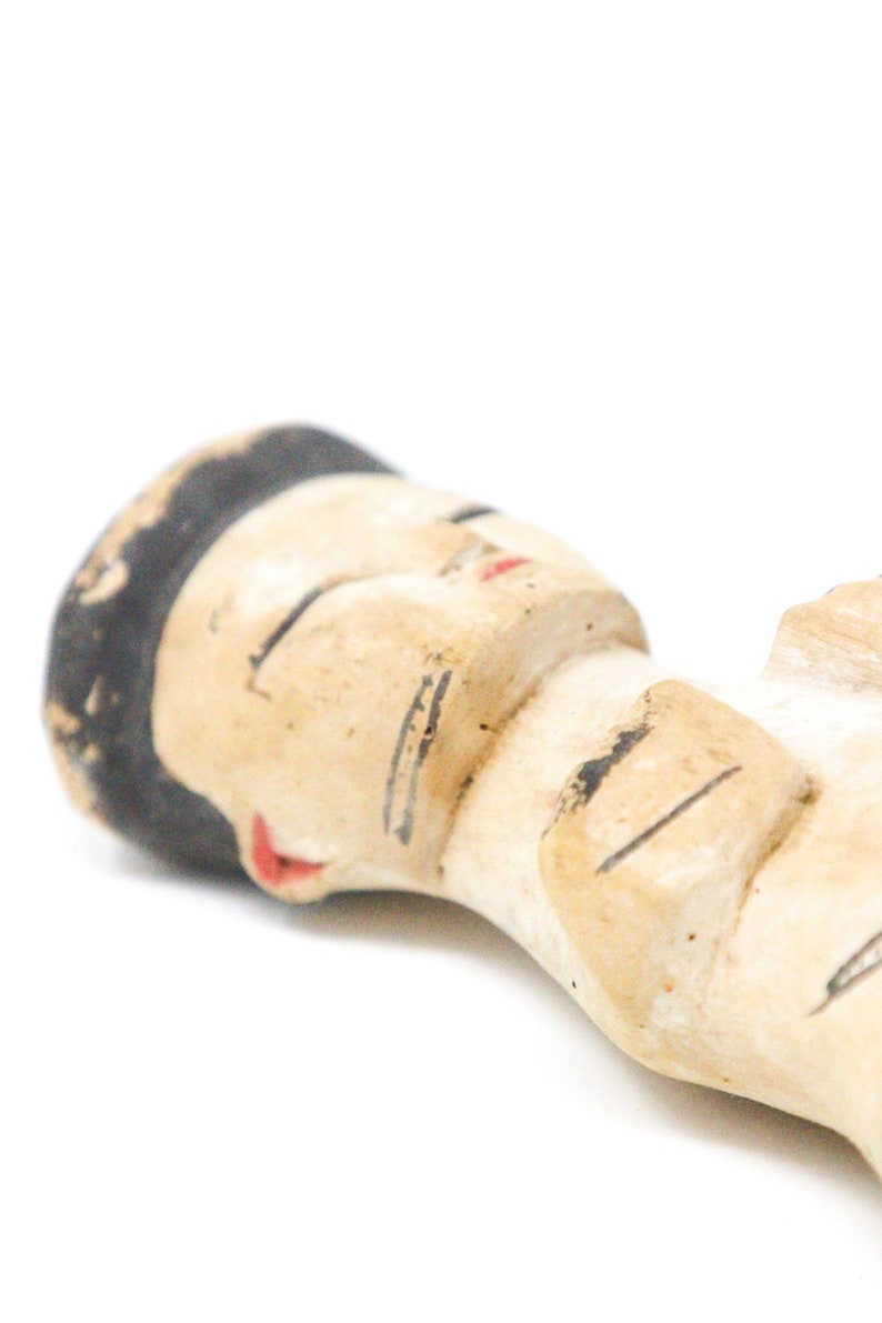 以下が含まれることがあります： 黒髪で目を閉じ、赤い口をした人の小さな手描きセラミック人形。人形は横向きに寝ていて、腕を組んでいます。