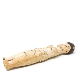 以下が含まれることがあります： 横たわっている人の木製の置物。置物は黒と赤のディテールでペイントされています。置物は薄い茶色の木でできています。