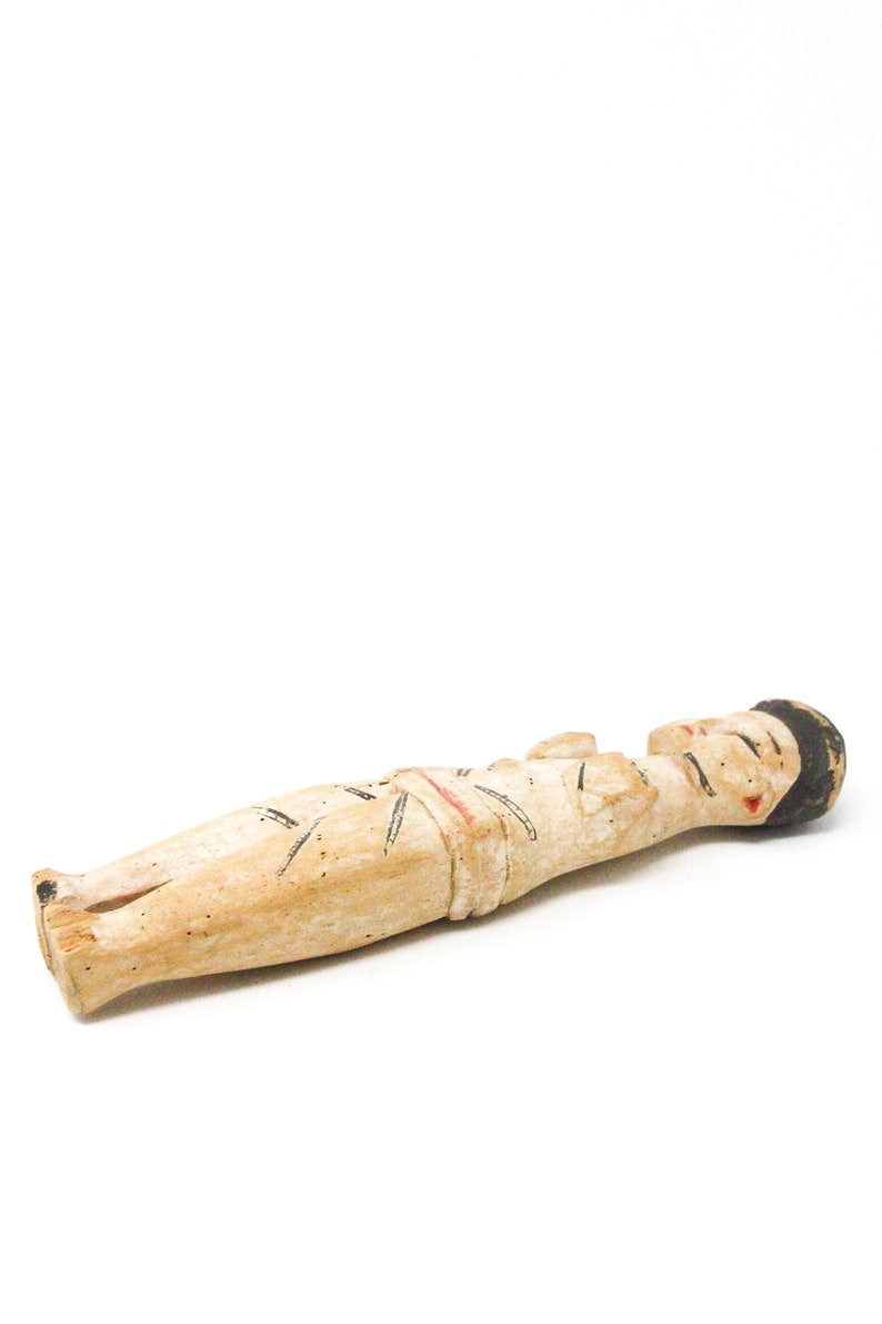 以下が含まれることがあります： 横たわっている人の木製の置物。置物は黒と赤のディテールでペイントされています。置物は薄い茶色の木でできています。