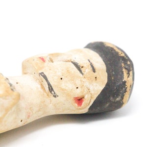 以下が含まれることがあります： 黒髪で目を閉じ、赤い唇をした人の手描きセラミック人形。人形は薄い茶色の粘土で作られており、素朴で手作り感のある外観です。