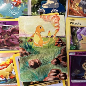 May include: A collection of Pokémon trading cards. The cards feature various characters, including Magikarp, Snorlax, Pikachu, and Mimikyu. One card depicts a Charmander in a grassy field with a fire. The cards are in English.
