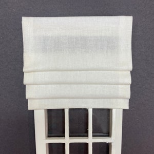 May include: White roman shade with a white wooden window frame with nine panes of glass.