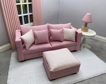 May include: A pink sofa with four white and pink pillows, a pink ottoman, and a white side table with a pink lamp. The sofa and ottoman are on a white rug.