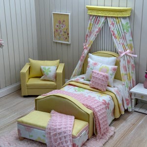May include: A miniature bedroom set with a yellow bed, armchair, and ottoman. The bed has a floral patterned comforter and canopy. A pink throw blanket and pillows add color. A small white nightstand holds a pink vase with flowers.