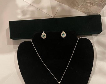 May include: A silver necklace and earrings set with a teardrop-shaped green gemstone surrounded by smaller clear gemstones.