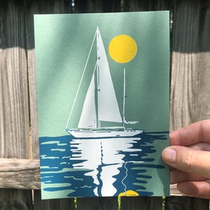 May include: A green and blue print of a sailboat on the water with a yellow sun in the sky.