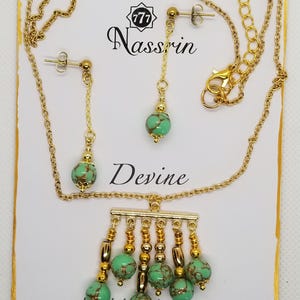 Può includere: Un set di collana e orecchini in oro con un ciondolo verde e oro. Il ciondolo presenta una barra con più fili di perline dorate e pietre verdi. Gli orecchini sono semplici cerchi d'oro con una pietra verde che pende da ciascuno. La carta recita "777 Nassrin Devine Morse Code with hidden Meaningful messages".