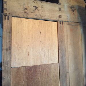 May include: A wooden cabinet with two doors and a shelf. The cabinet is made of light brown wood and has a simple design.
