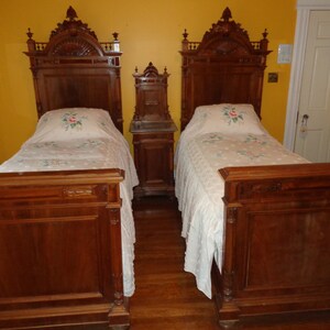 May include: Two antique twin-sized beds with ornate wooden headboards and footboards. The beds are made with dark wood and have white linens with floral embroidery.