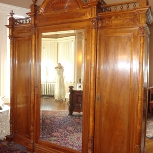 May include: A large, antique wooden armoire with a mirrored door and two solid wood doors. The armoire has intricate carvings and a decorative top.