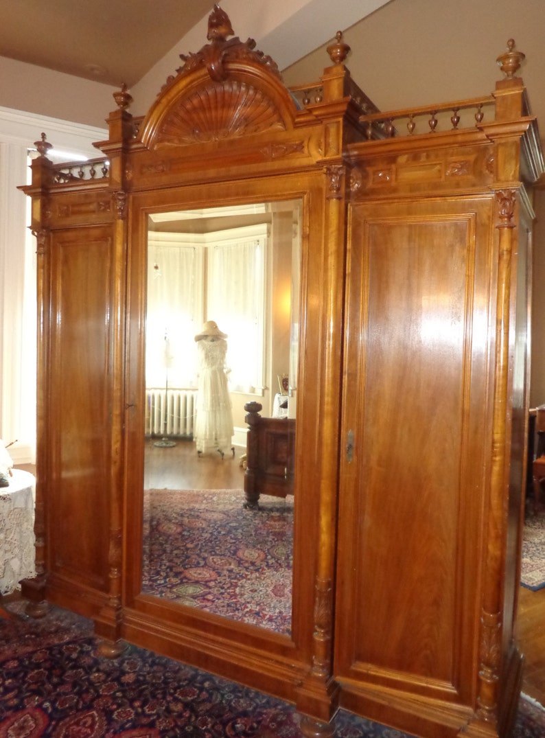 May include: A large, antique wooden armoire with a mirrored door and two solid wood doors. The armoire has intricate carvings and a decorative top.