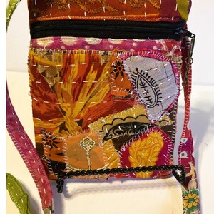 K&ouml;nnte beinhalten: Eine bunte Patchwork-Umh&auml;ngetasche mit schwarzem Rei&szlig;verschluss und Riemen. Die Tasche hat verschiedene Stoffflicken in Orange-, Rot-, Gelb- und Rosat&ouml;nen, die mit wei&szlig;em Faden zusammengen&auml;ht sind. Der Riemen ist eine Kombination aus gr&uuml;nem, rosa und gemustertem Stoff.