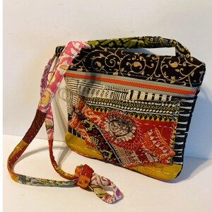 May include: A patchwork shoulder bag with a variety of patterned fabrics in black, white, red, yellow, and orange. The bag has a long strap and a small handle. The design includes floral and geometric patterns, with a decorative patch on the front.