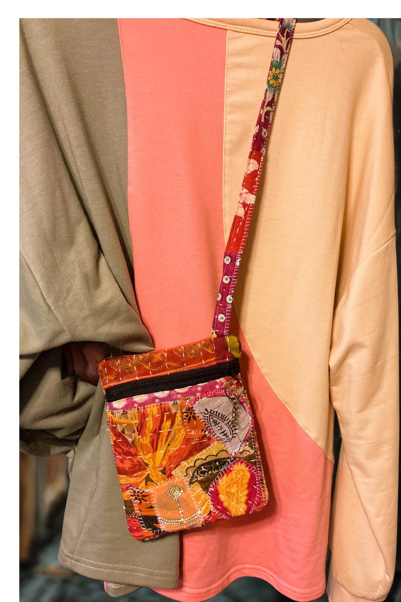 K&ouml;nnte beinhalten: Eine bunte Patchwork-Umh&auml;ngetasche mit floralem Design. Die Tasche hat einen schwarzen Rei&szlig;verschluss und einen gemusterten Riemen. Die Tasche besteht aus verschiedenen Stoffen in Orange-, Rot-, Rosa- und Gelbt&ouml;nen.