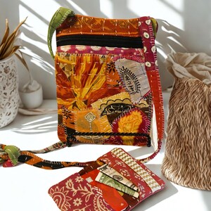 K&ouml;nnte beinhalten: Eine Patchwork-Umh&auml;ngetasche und eine passende Geldb&ouml;rse. Die Tasche hat eine Mischung aus orangefarbenen, gelben und roten Stoffen mit einem schwarzen Rei&szlig;verschluss und einem gr&uuml;nen Riemen. Die Geldb&ouml;rse ist rot mit einem Paisley-Muster und enth&auml;lt Karten und Bargeld.