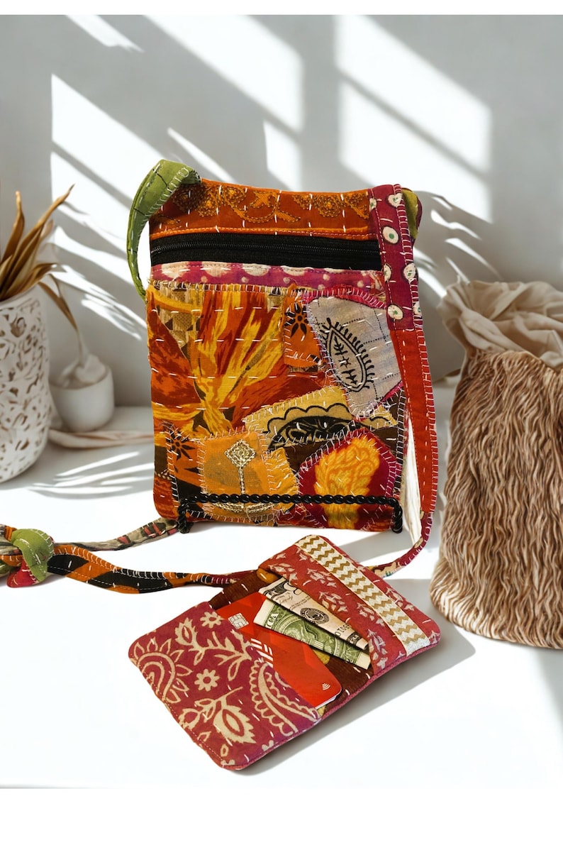 K&ouml;nnte beinhalten: Eine Patchwork-Umh&auml;ngetasche und eine passende Geldb&ouml;rse. Die Tasche hat eine Mischung aus orangefarbenen, gelben und roten Stoffen mit einem schwarzen Rei&szlig;verschluss und einem gr&uuml;nen Riemen. Die Geldb&ouml;rse ist rot mit einem Paisley-Muster und enth&auml;lt Karten und Bargeld.