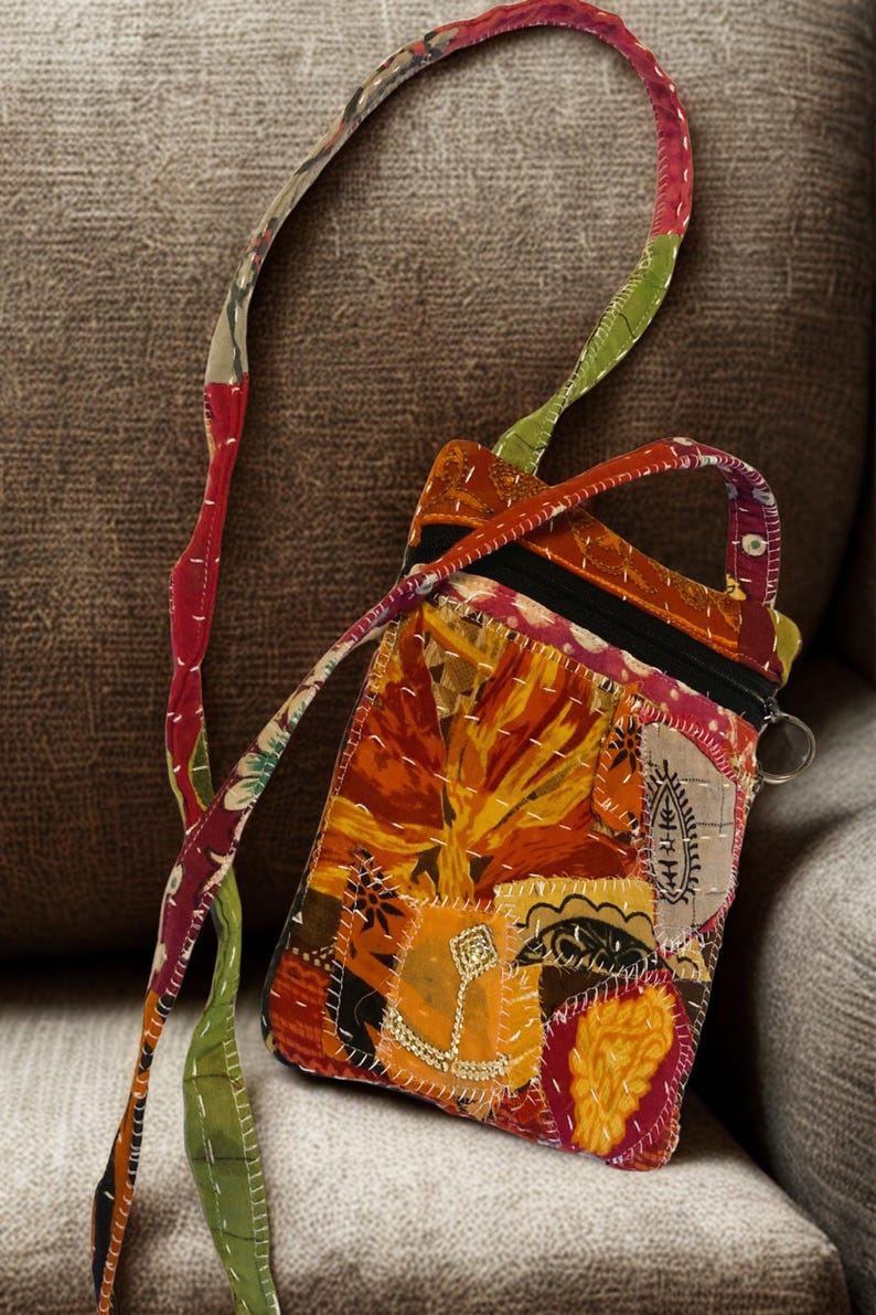 K&ouml;nnte beinhalten: Eine Patchwork-Umh&auml;ngetasche mit floralem Design in Orange-, Gelb- und Rott&ouml;nen. Die Tasche hat einen schwarzen Rei&szlig;verschluss und einen langen Riemen mit einer Mischung aus Mustern und Farben. Die Tasche ist ca. 15 cm breit und 20 cm hoch.