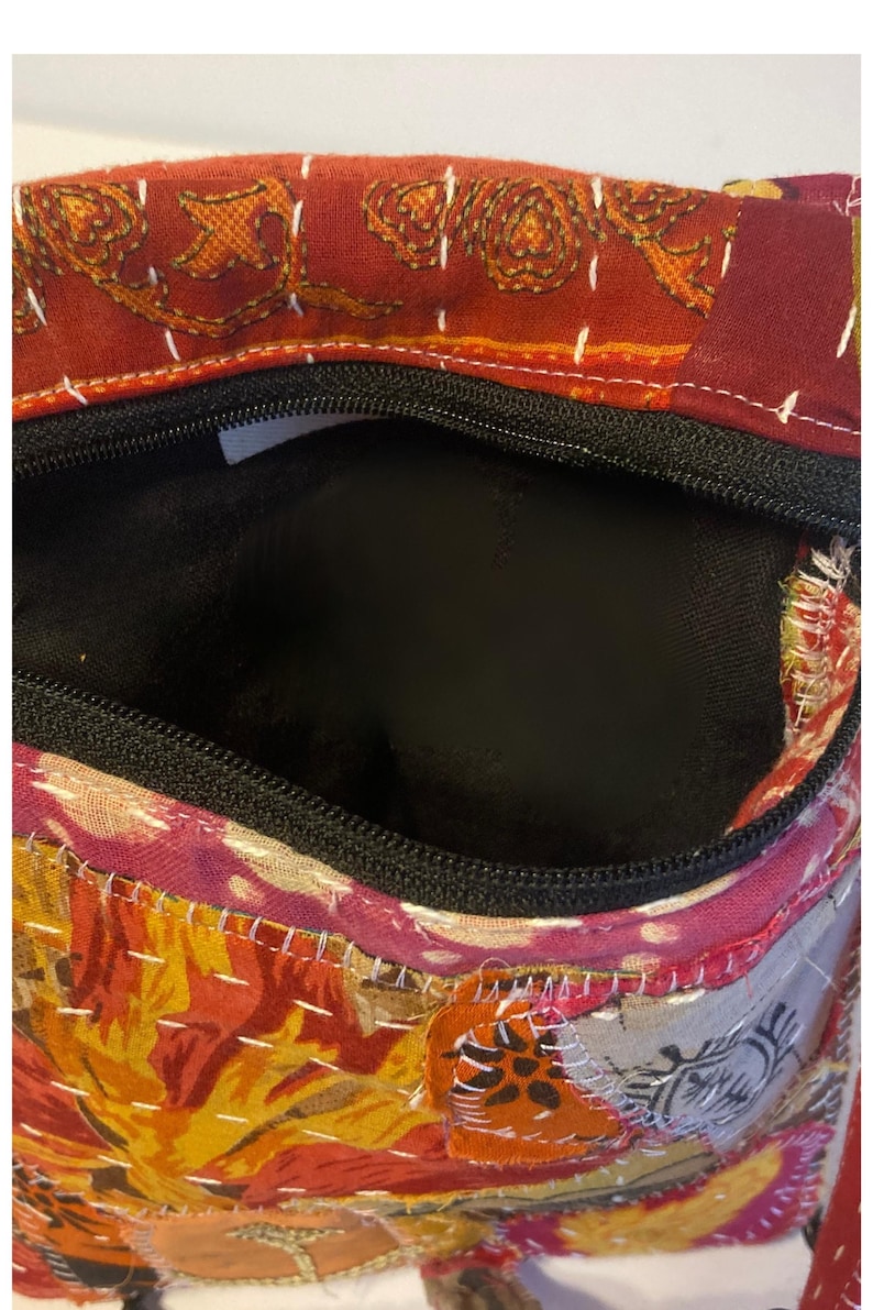 K&ouml;nnte beinhalten: Eine farbenfrohe, offene Handtasche mit schwarzem Rei&szlig;verschluss und Innenraum. Die Tasche hat ein Patchwork-Design mit Blumen- und geometrischen Mustern in Rot-, Orange- und Rosat&ouml;nen. Wei&szlig;e N&auml;hte akzentuieren den Stoff.