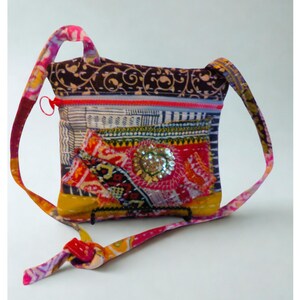 May include: A colorful, patchwork crossbody bag with a long strap. The bag features a mix of patterned fabrics in red, yellow, blue, and brown, with a central embellished design. The strap is made of matching fabric.