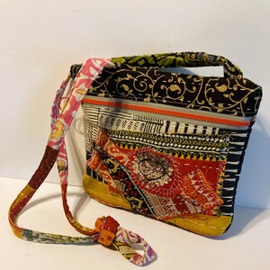 May include: A patchwork shoulder bag with a variety of patterns and colors. The bag features a black background with gold floral designs, a yellow base, and a red and orange patch with sequins. The strap is multi-colored.