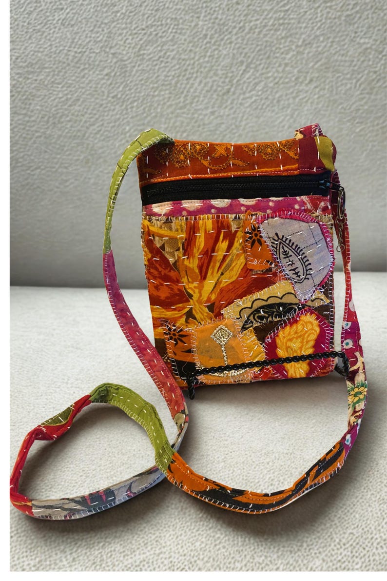 K&ouml;nnte beinhalten: Eine Patchwork-Umh&auml;ngetasche mit farbenfrohem Design. Die Tasche hat eine Mischung aus orangefarbenen, gelben und rosa Stoffen mit einem schwarzen Rei&szlig;verschluss und Riemen. Der Riemen ist eine Mischung aus gr&uuml;nen, roten und orangefarbenen Stoffen.