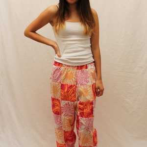 May include: A woman wearing a white vest top and pink and orange patterned pyjama trousers with a floral design.