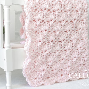 May include: A pink crocheted baby blanket draped over a white crib. The blanket has a scalloped edge and a delicate stitch pattern. The text 'CALLI CHIC Baby' is visible in the bottom right corner of the image.
