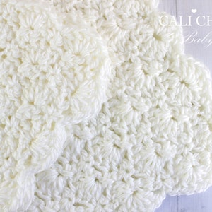 May include: A white crocheted baby blanket with a scalloped edge. The blanket is made with a delicate stitch pattern and is soft and cozy.