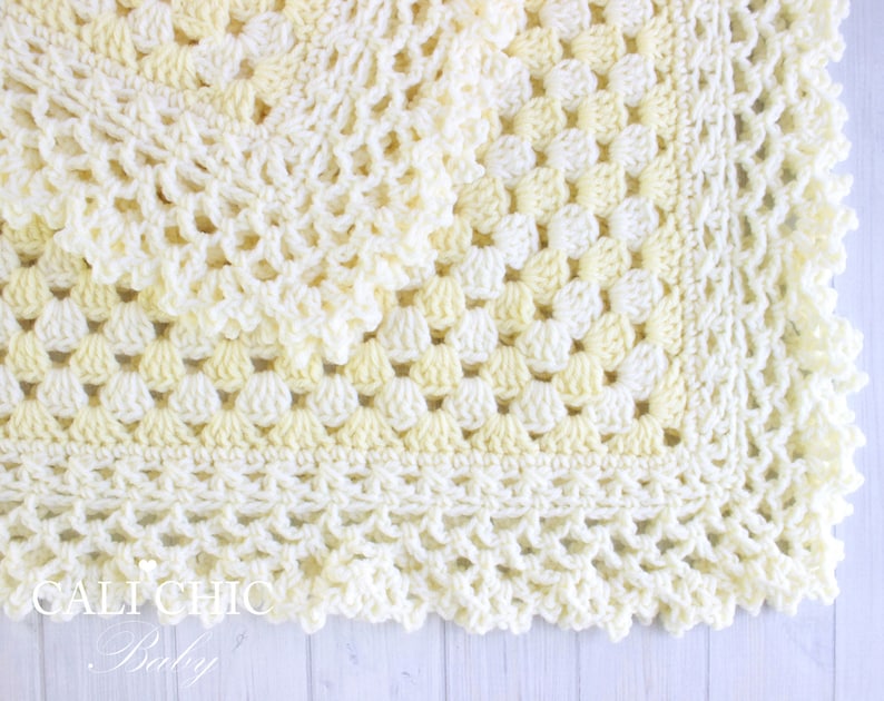 May include: A crocheted baby blanket in shades of white and yellow with a scalloped edge.