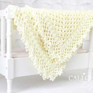 May include: A crocheted baby blanket in a pale yellow color, with a delicate lace pattern. The blanket is draped over a white crib.