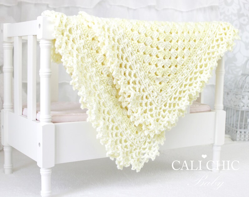 May include: A crocheted baby blanket in a pale yellow color, with a delicate lace pattern. The blanket is draped over a white crib.