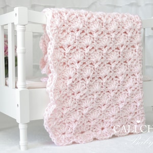 May include: A pink crocheted baby blanket with a scalloped edge, draped over a white crib.