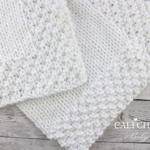 May include: White knitted baby blanket with a textured stitch pattern. The blanket is folded in half and has a "CALI CHIC Baby" logo in the bottom right corner.