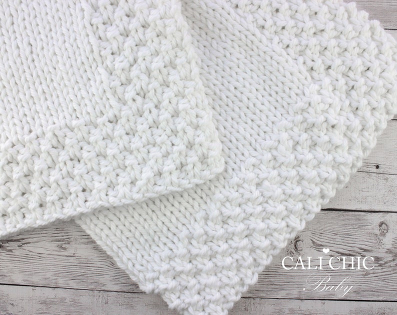 May include: White knitted baby blanket with a textured stitch pattern. The blanket is folded in half and has a "CALI CHIC Baby" logo in the bottom right corner.