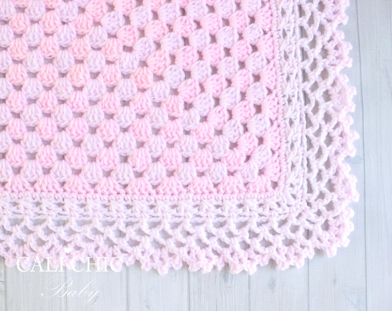 May include: A pink and white crocheted baby blanket with a delicate scalloped edge.