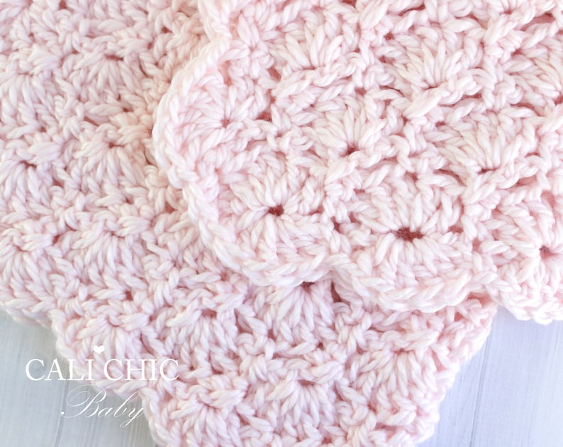 May include: A close-up of a pink crocheted baby blanket with a delicate, lacy pattern. The blanket is made with soft yarn and has a gentle, feminine feel.