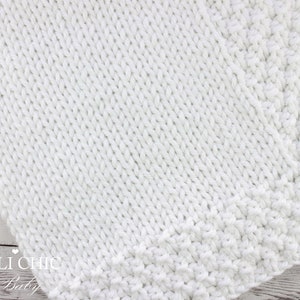 May include: White knitted baby blanket with a textured stitch pattern. The blanket has a simple border around the edges.
