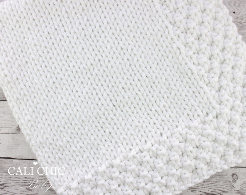 May include: White knitted baby blanket with a textured stitch pattern. The blanket has a simple border around the edges.