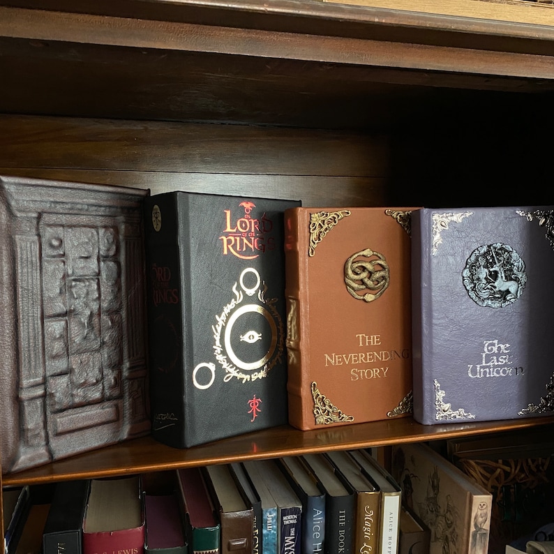 The Neverending Story special illustrated edition, on bookshelf from left, Chronicles of Narnia (leather wardrobe), The Lord of the Rings (black leather, Neverending Story, and the Last Unicorn(light purple leather)