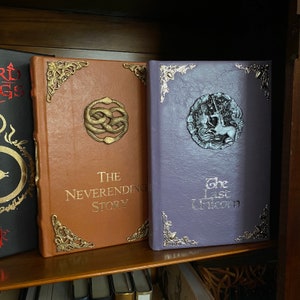 Photo shows special editions on bookshelf, from left to right, Lord of the Rings black leather book, The Neverending Story in cognac brown leather, and The Last Unicorn in light purple leather