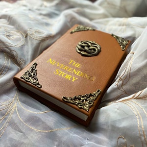 The Neverending Story book, leather bound, gold title, aged gold filigree corner pieces and ouroboros, two snakes entwined to create the "Auryn".