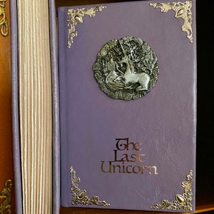 Photo shows the pages facing out to show deckled edges next to another copy of the Last Unicorn book in light purple leather with silver adornments