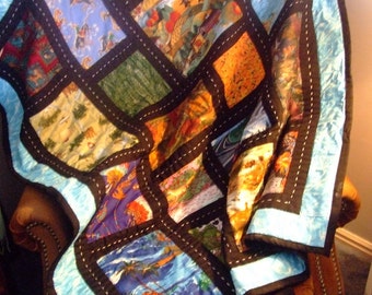 May include: A blue and black patchwork quilt with a variety of colorful patterns. The quilt is made of different fabrics and has a black border with white stitching. The quilt is folded and draped over a brown leather armchair.