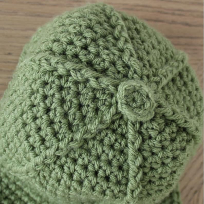 Puede incluir: Un gorro de punto de color verde con un dise&ntilde;o texturizado y un peque&ntilde;o pomp&oacute;n redondo en la parte superior.
