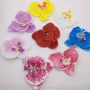 May include: Assortment of artificial orchid flowers in various colors, including white, pink, yellow, red, blue, and pink with white speckles. The flowers are made of fabric and have a realistic appearance.