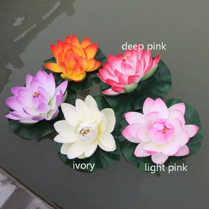 May include: Five artificial lotus flowers in different colours: ivory, light pink, deep pink, purple, and orange. The flowers are floating on water with green leaves.