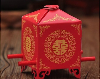 May include: Red and gold paper box shaped like a traditional Chinese wedding sedan chair. The box has a double happiness symbol in gold on the front.